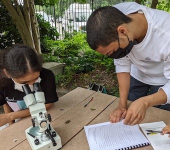 man helping girl with a microscope.
